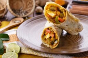 A picture of a hot and freshly made Paneer Tikka Roll, filled with tender marinated paneer cubes, crisp lettuce, juicy tomatoes and tangy chutneys, all wrapped in a warm roti or flatbread