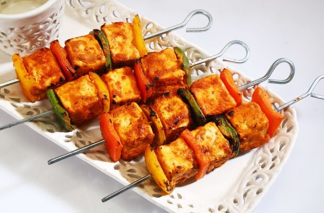 A close-up photo of a plate of sizzling Paneer Tikka, with juicy marinated paneer cubes skewered and grilled to perfection with colorful bell peppers and onions